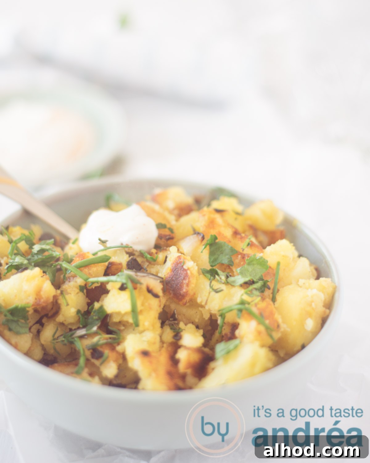Close-up of crispy pan-fried potatoes with green herbs in a serving dish, with a small bowl of garlic yogurt sauce beside them.