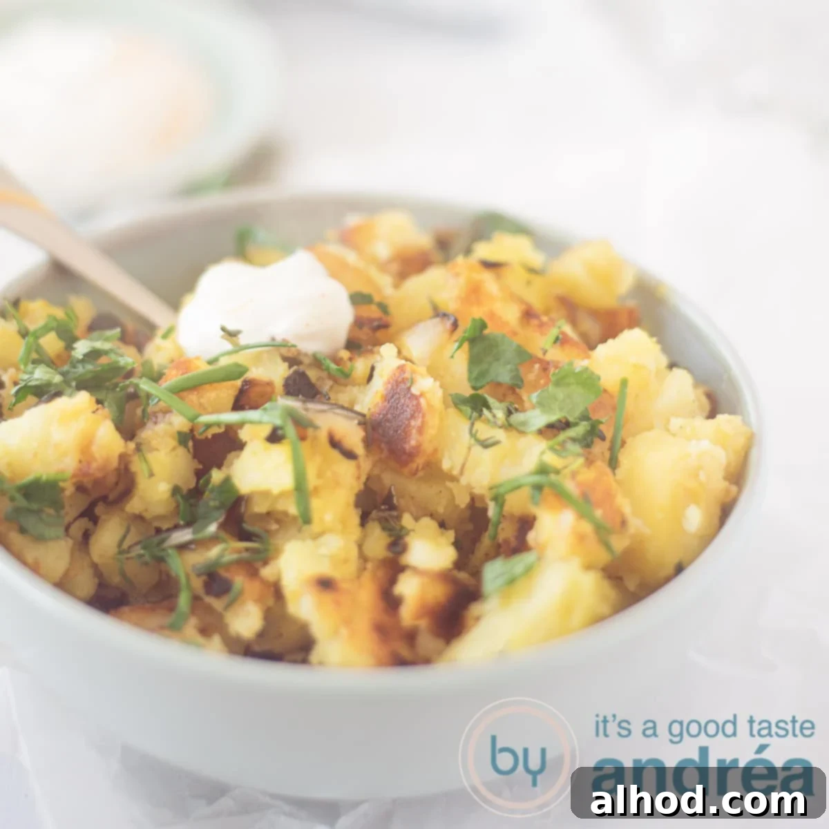 A square photo of a blue bowl filled with pan-fried potatoes, curry, and herbs, served with a dollop of garlic yogurt sauce.