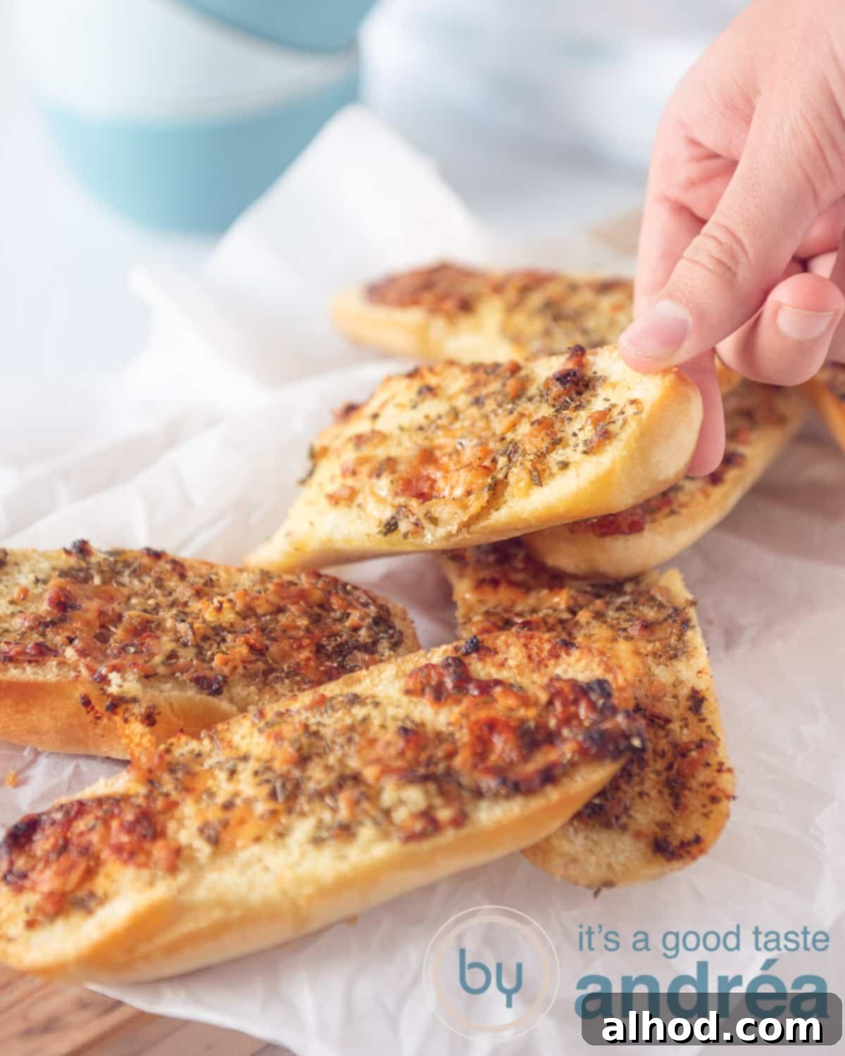 Ultimate Parmesan Garlic Bread 2 An elevation photo with sandwiches topped with garlic with Parmesan cheese. A hand picks up a sandwich. Everything on a white background, highlighting the golden-brown crust and melted cheese.