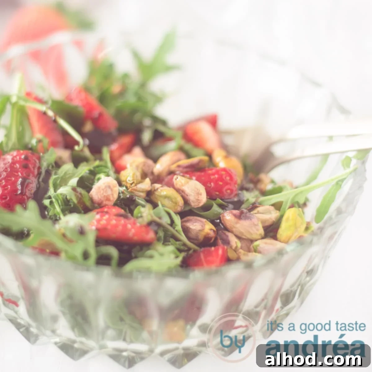 Strawberry Pistachio Salad 6 A square photo with part of a glass bowl filled with arugula, strawberries and pistachio nuts