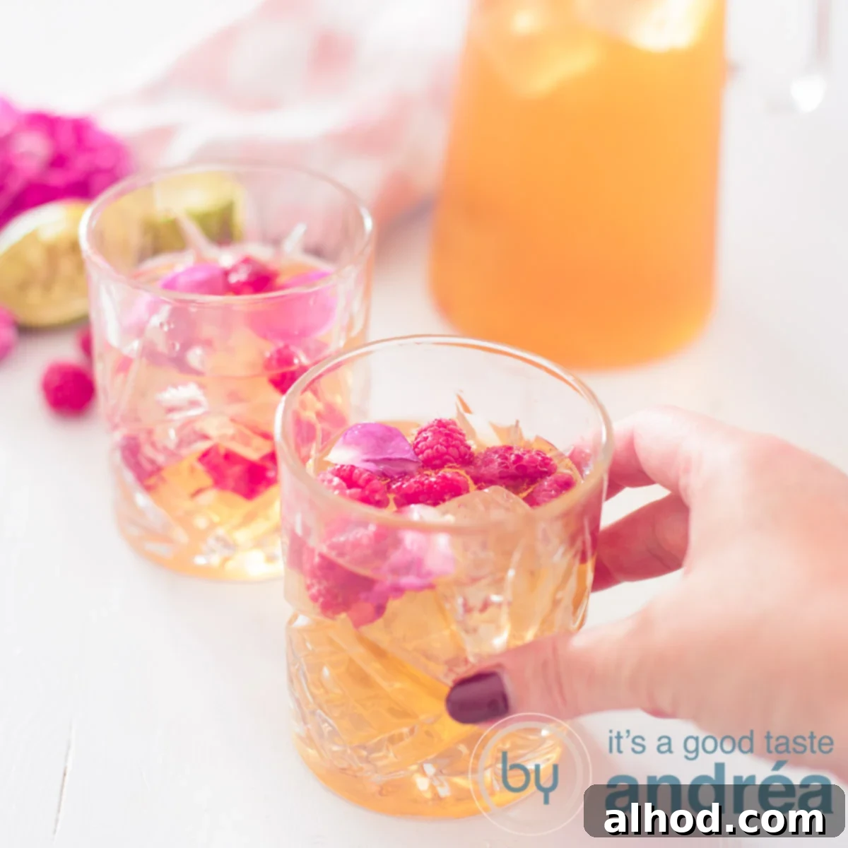 Aromatic Rose & Zesty Lime Iced Tea 6 A square picture with lime rose and raspberry iced tea, two glasses and a jar diagonally. A hand is taking the first glass.