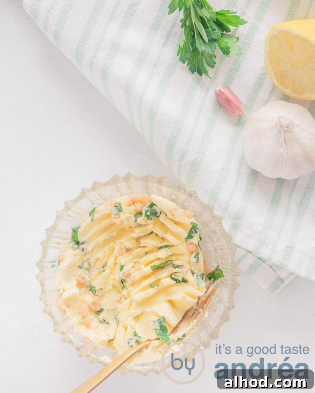 A top photo in the left bottom, glass bowl filled with garlic herb butter. Top right a green and white towel, topped with garlic, parsley and lemon