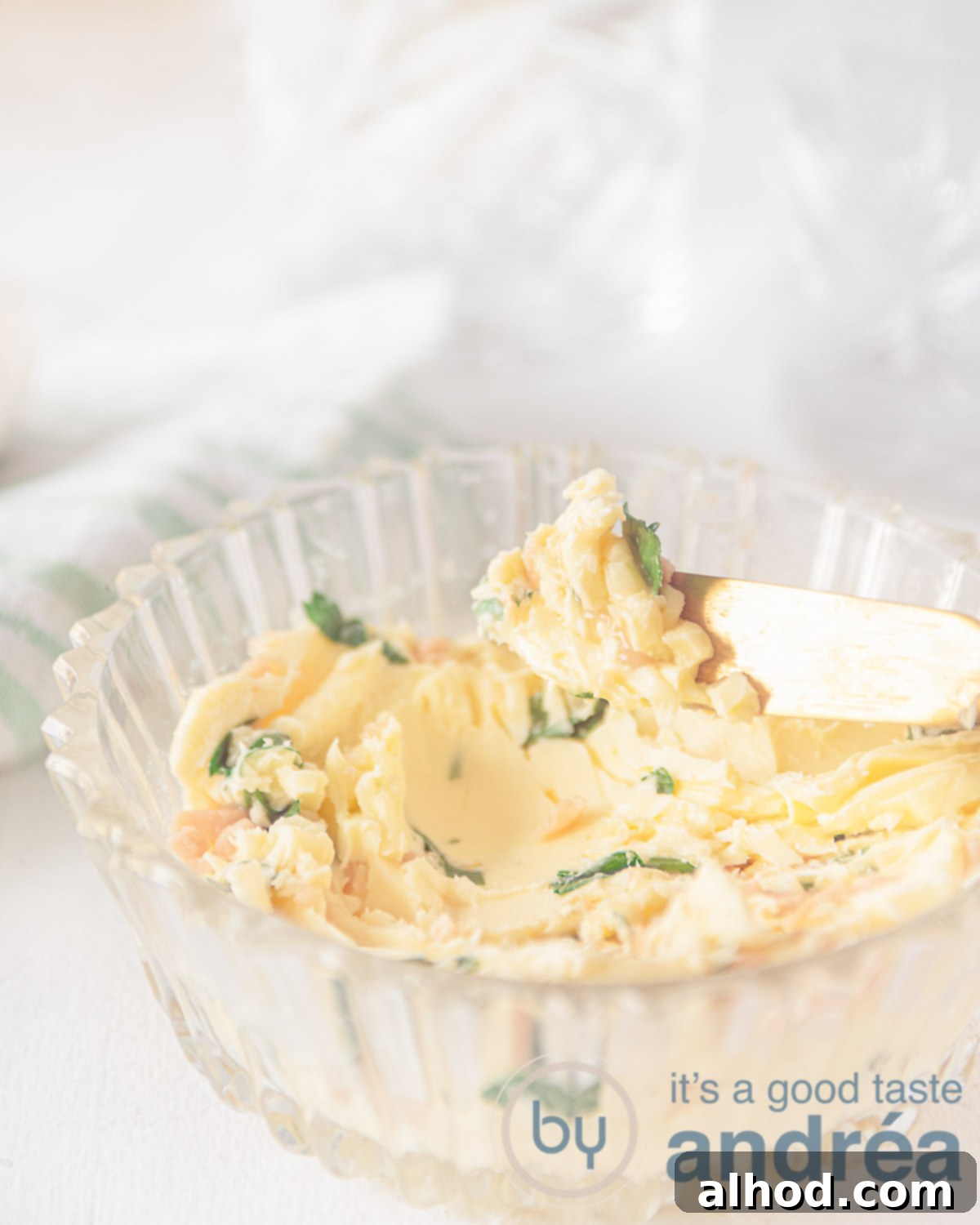Homemade garlic butter in a glass bowl. A golden knife taking a smear. A white background