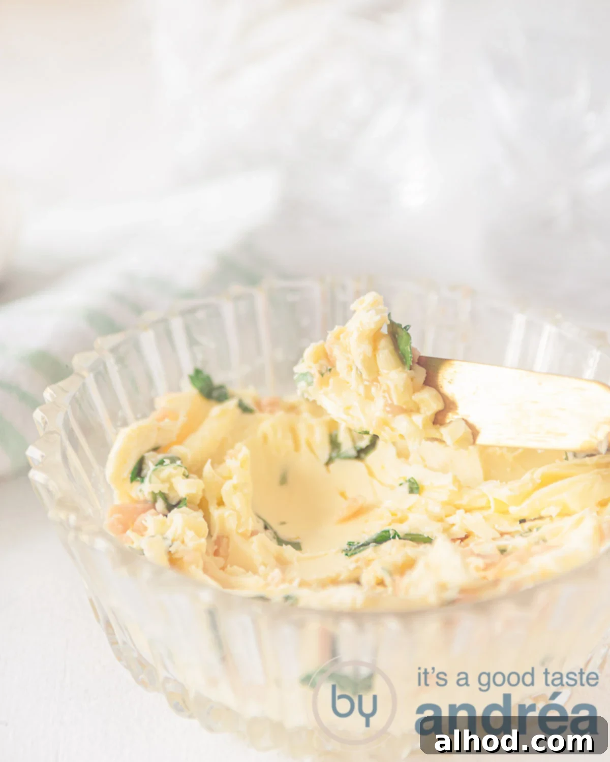 Effortless Garlic Herb Butter 5 Homemade garlic butter in a glass bowl. A golden knife taking a smear. A white background