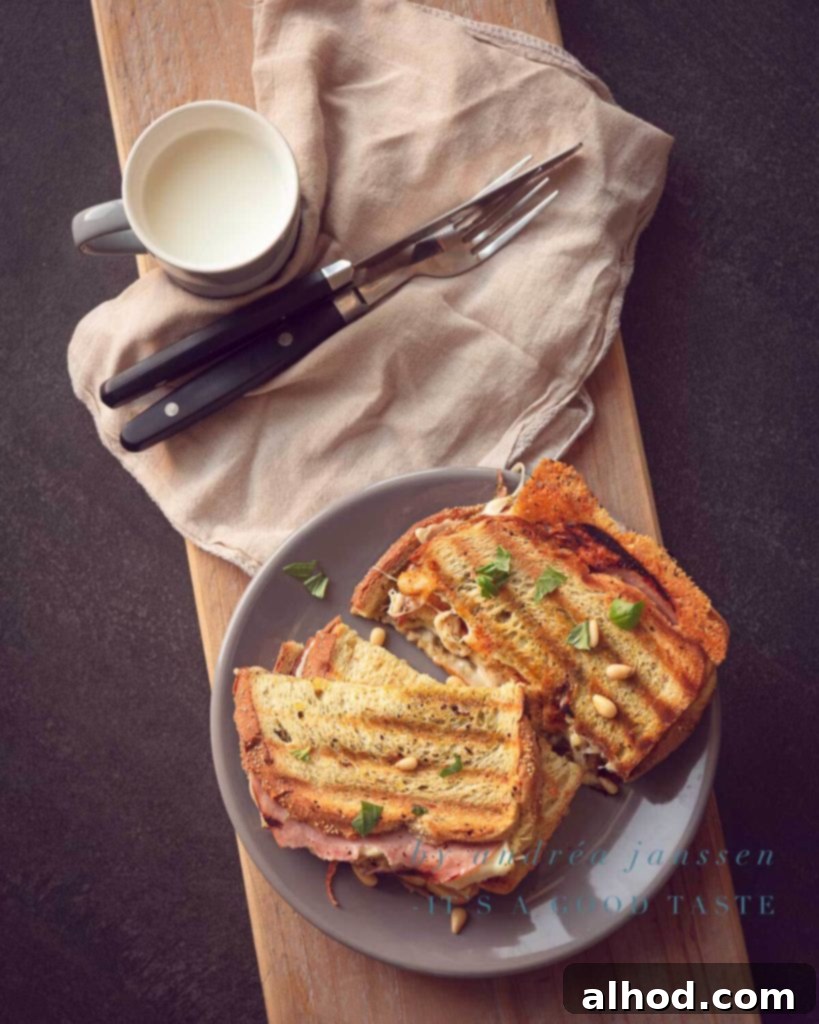 Pesto Melt 2 A perfectly golden-brown grilled cheese sandwich with pesto, ham, and pine nuts, slightly opened to reveal melted cheese and vibrant green pesto.