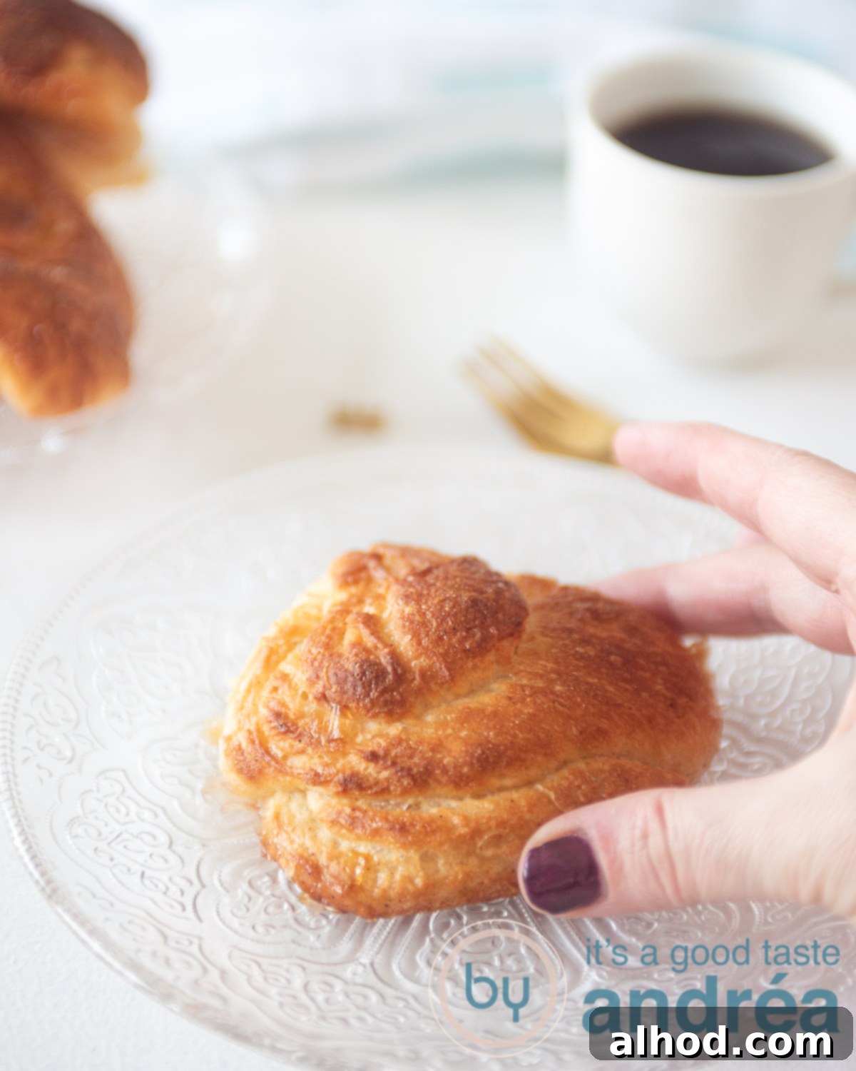 Dutch Cinnamon Swirls 5 A hand reaching for a Zeeuwse bolus from a glass plate, with a cup of coffee and more bolussen in the background, set for an enjoyable moment.