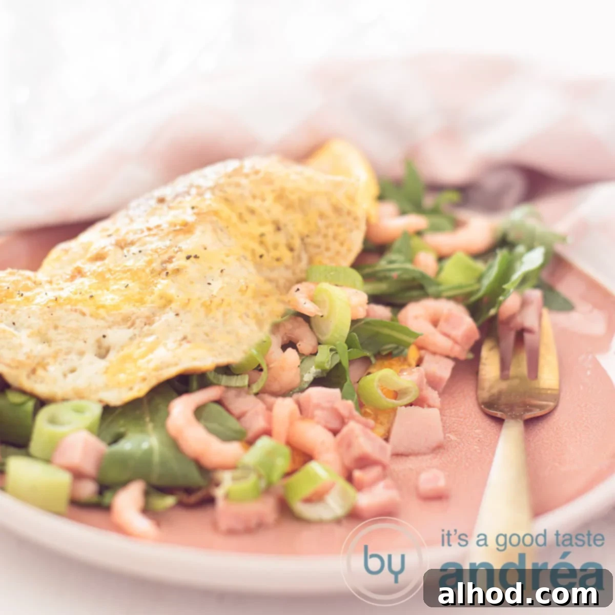 Savory Shrimp Omelette 6 A square photo with a pink plate in the foreground, with a filled omelette with arugula, spring onions, shrimps and ham. In the background a pink, white tea towel.
