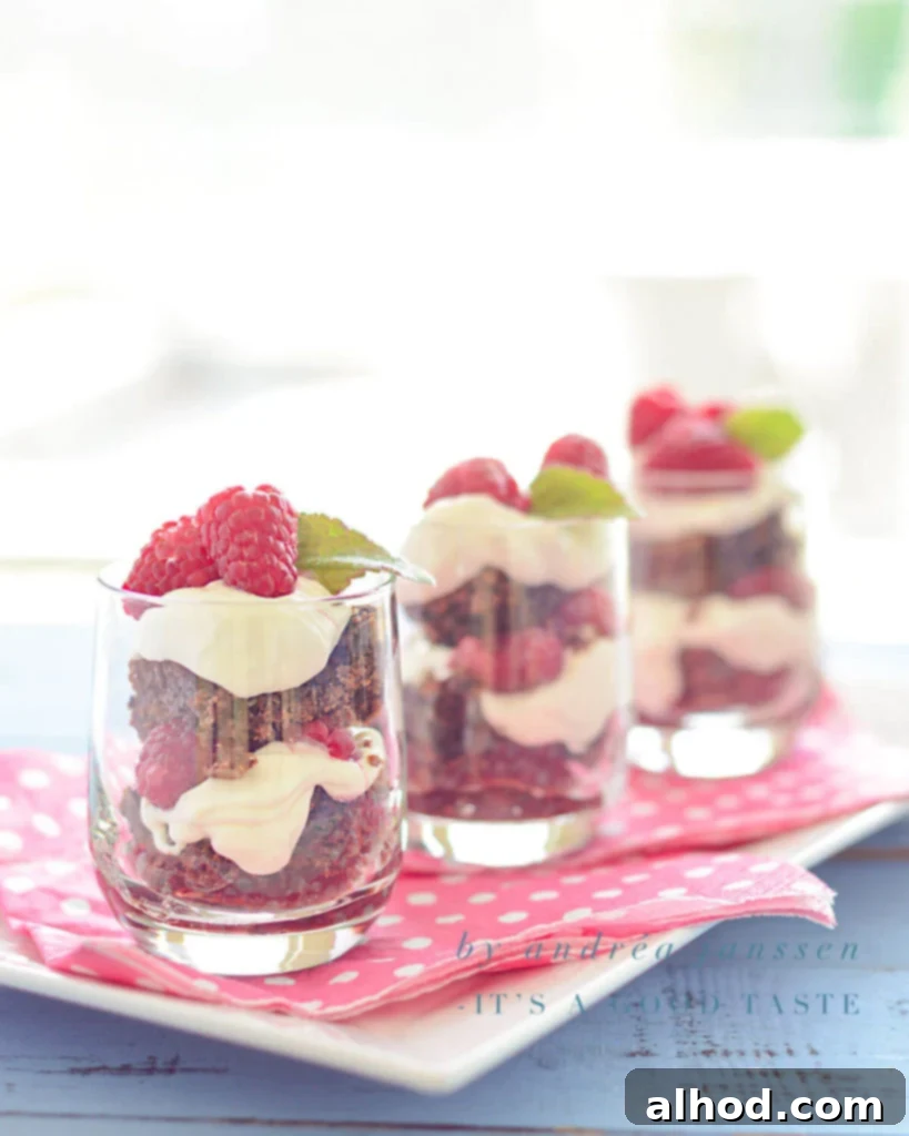 Raspberry Brownie Tiramisu Bliss 2 Three elegant glasses filled with layers of Raspberry Brownie Tiramisu, garnished with fresh raspberries, on a soft pink napkin.