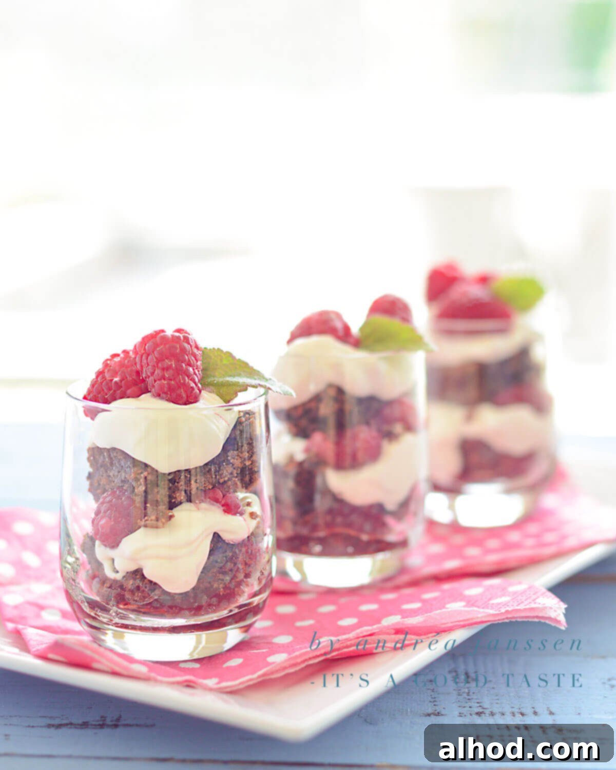 Raspberry Brownie Tiramisu Bliss 3 Three glasses filled with layered Raspberry Brownie Tiramisu on a pink napkin, garnished with fresh raspberries.