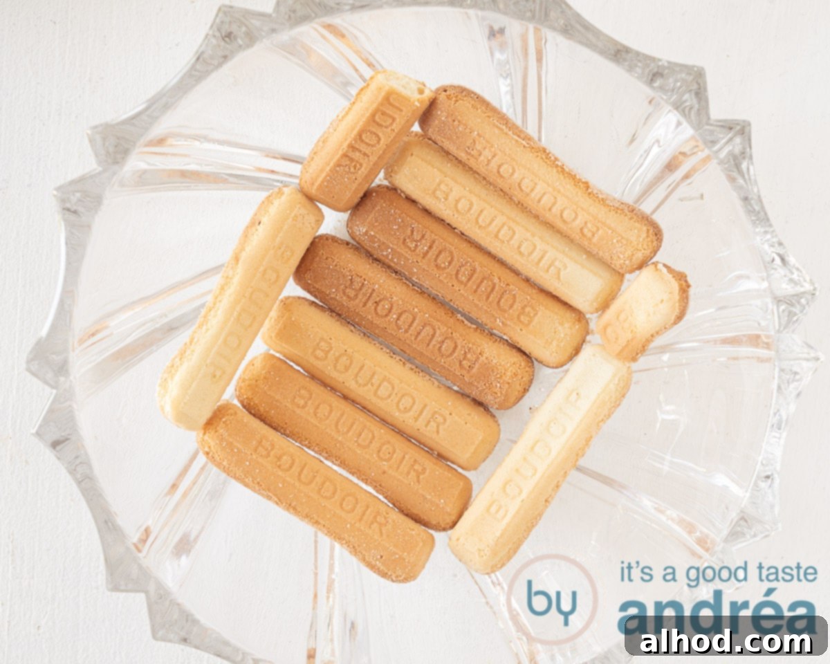 Ladyfingers carefully arranged to cover the bottom of a glass trifle bowl, forming the first layer.