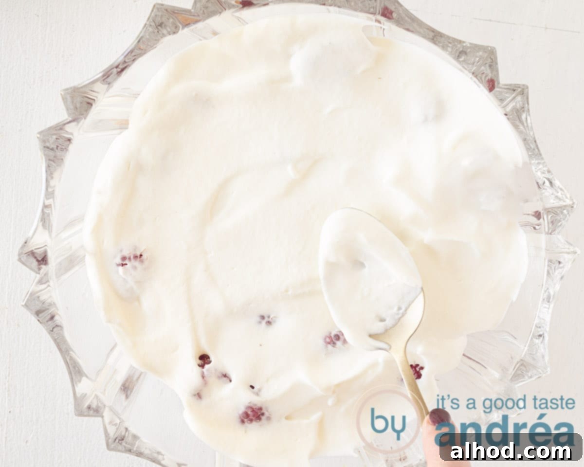 A thick layer of smooth vanilla whipped cream covering the raspberries, ready to be garnished and chilled.