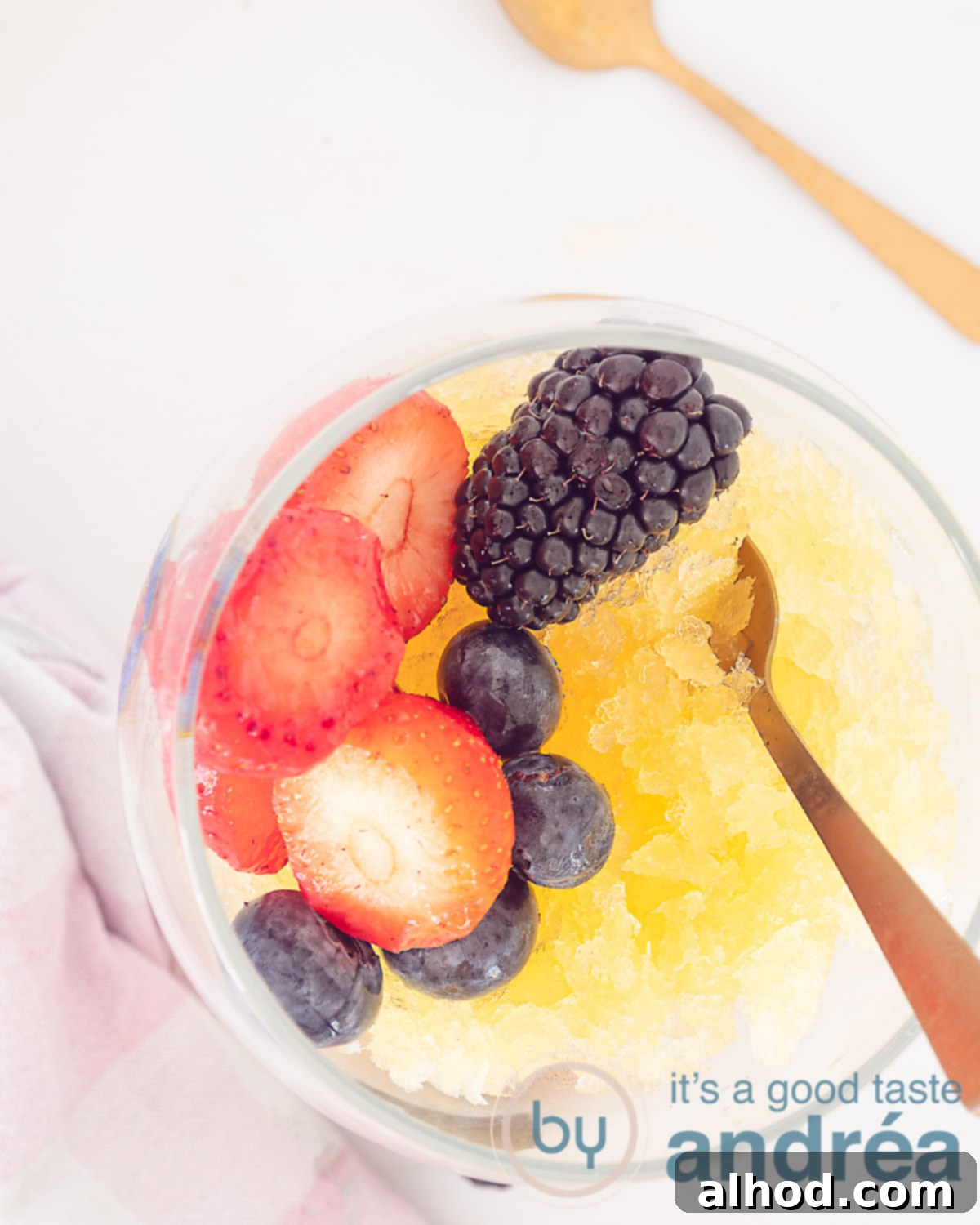 A height photo looking at the top of a glass filled with orange beer granita and fresh fruit. Two golden spoons.