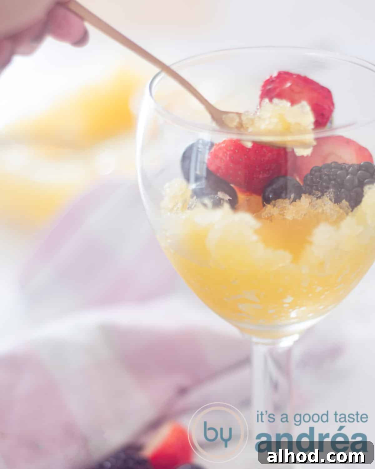 Hoppy Frost 6 A goblet filled with fresh beer ice with orange. A garnish of fresh fruit. A golden spoon takes a bite. A white background with a pink and white tea towel