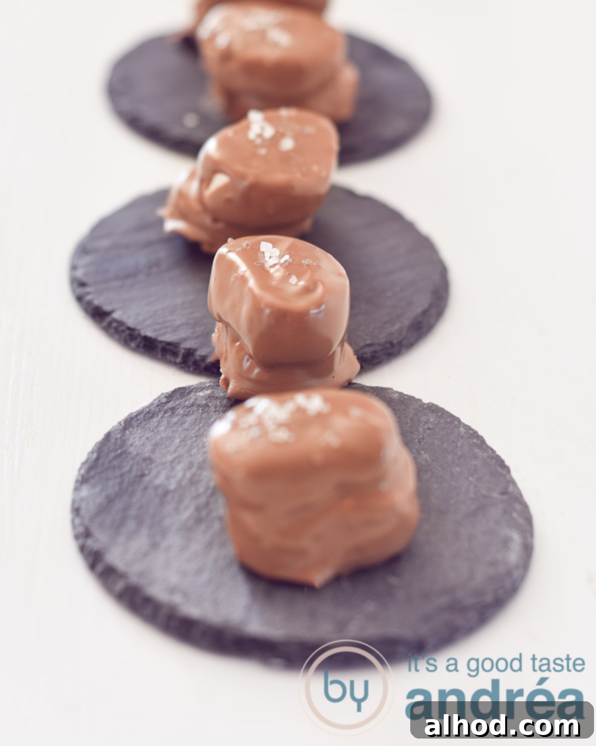 Beer-Spiked Chocolate Marshmallows with Sea Salt 2 Four delicious chocolate-dipped beer bonbons with sea salt, arranged in a row on a rustic stone plate against a clean white background.