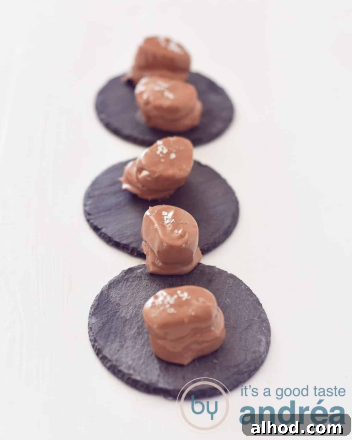 Boozy Chocolate Marshmallows with a Salty Kiss 3 An elevation photo with three slate coasters in a row and five beer chocolates with sea salt on them. Everything on a white background.