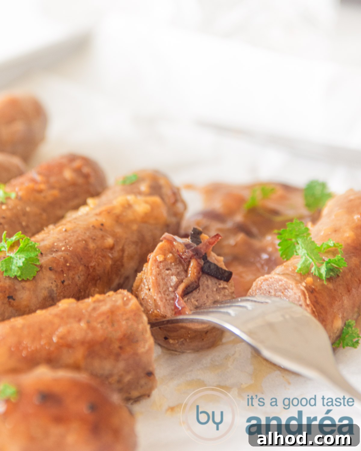 Beer-Braised Brats with Caramelized Onions 3 A close-up of several juicy bratwurst simmering in a rich beer and onion sauce. One bratwurst is cut open, revealing its tender interior, with a fork gently piercing it. Fresh parsley garnishes the dish, highlighting its appeal.