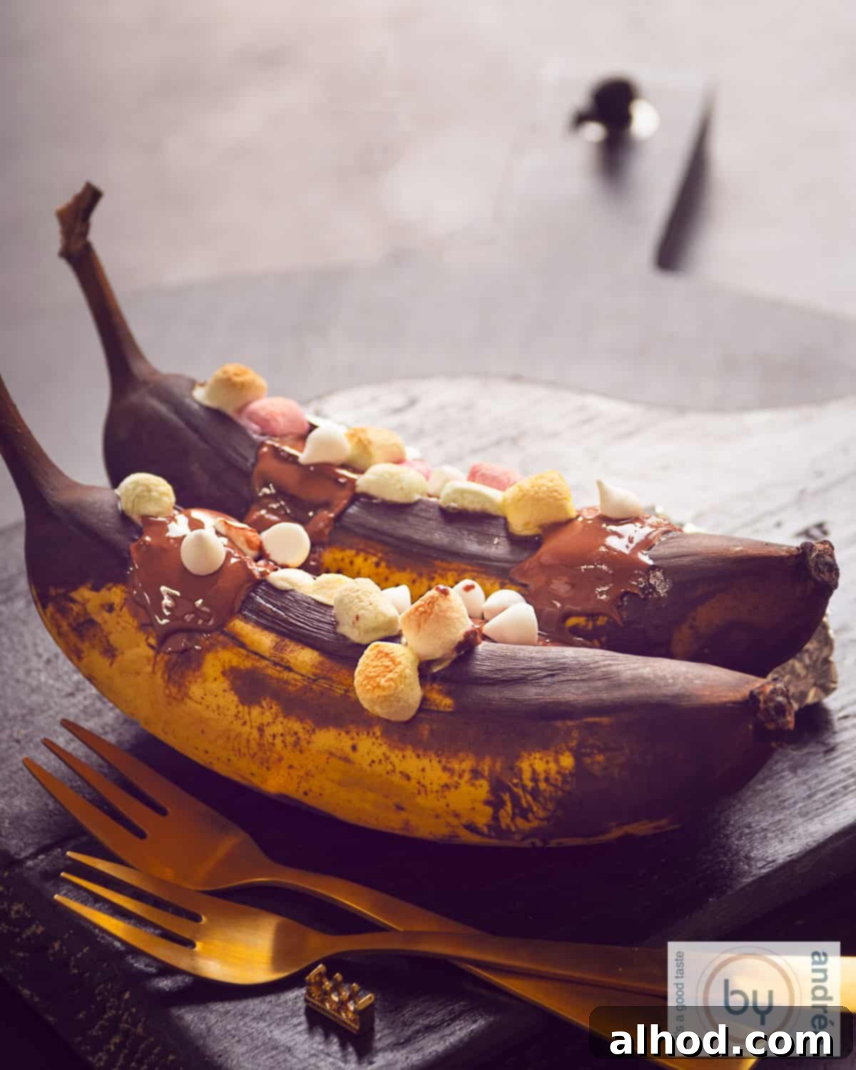 Two bananas on a wooden board, grilled and filled with whiskey, marshmallows and chocolate