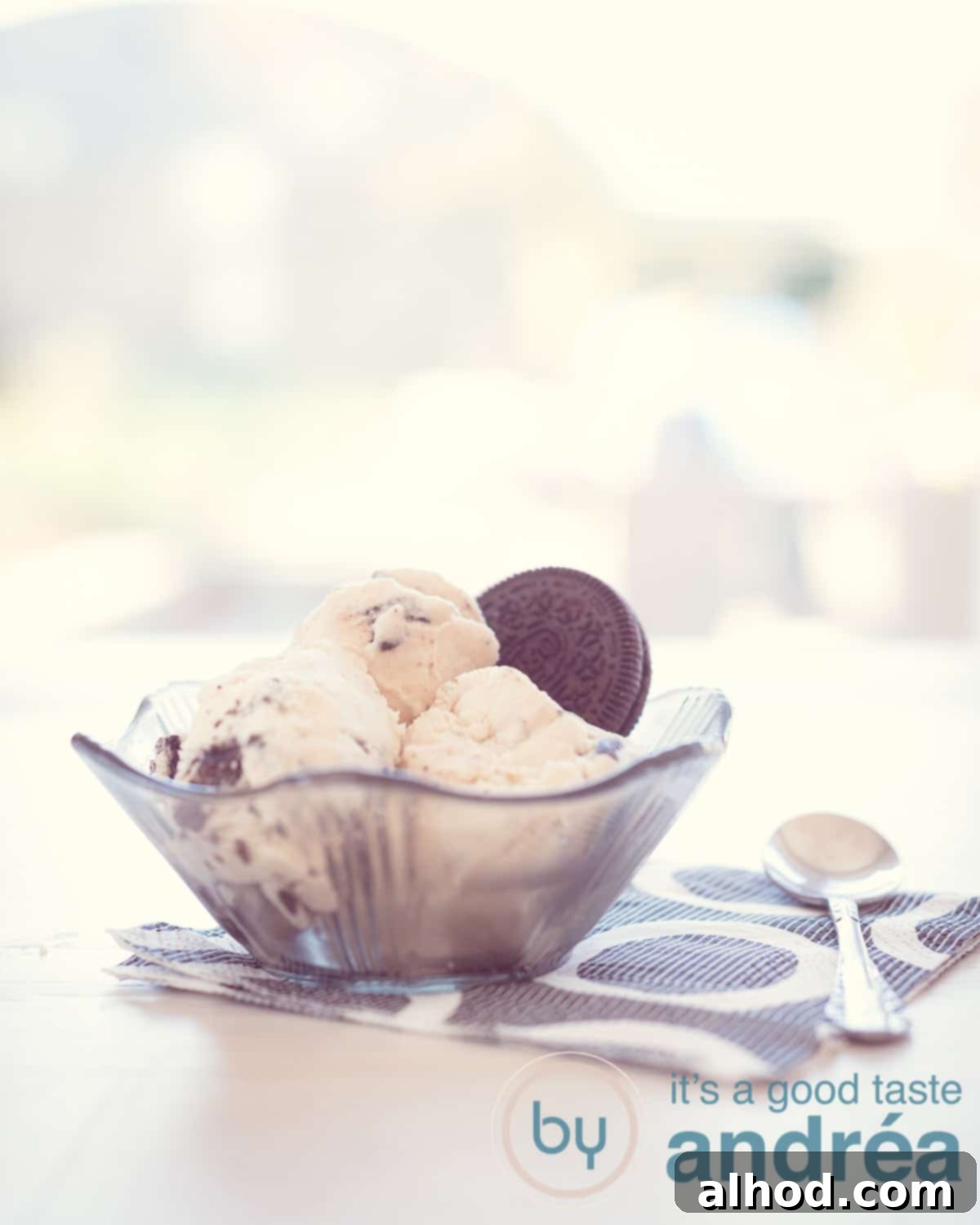 Three generous scoops of homemade Oreo gelato in a black glass dish, garnished with a whole Oreo cookie, resting on a white background with a stylish black and white striped napkin.