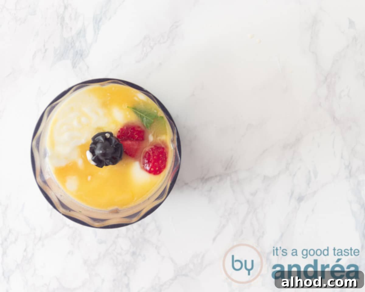 Zesty Berry Orange Blend 6 All smoothie ingredients, including Greek yogurt, fresh orange juice, quartered strawberries, mint leaves, and a spoonful of honey, are combined in a blender jar.