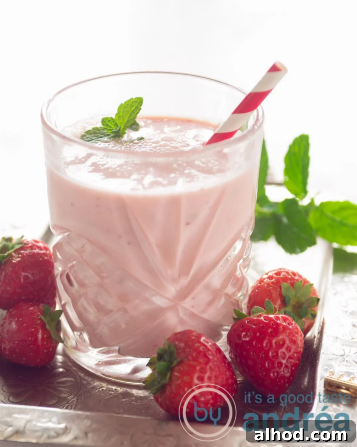 Zesty Berry Orange Blend 8 A beautifully presented glass of strawberry yogurt smoothie, garnished with a fresh strawberry and a sprig of mint, ready to be enjoyed.