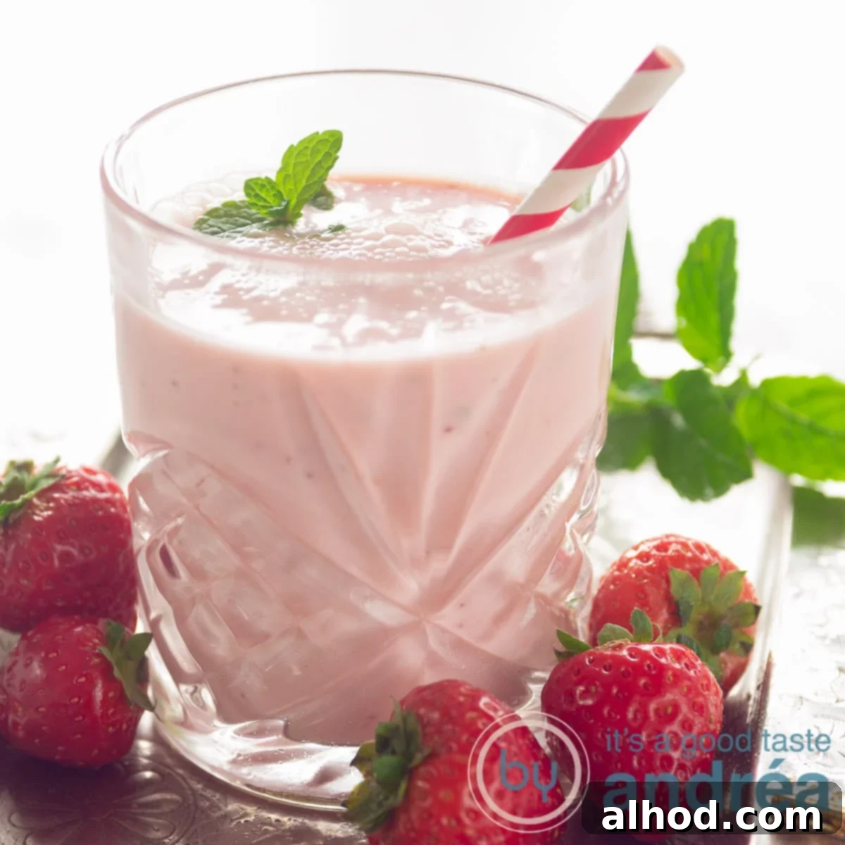 Zesty Berry Orange Blend 9 square photo with a glass filled with a strawberry orange yogurt smoothie, a red straw and surrounded with fresh strawberries and mint