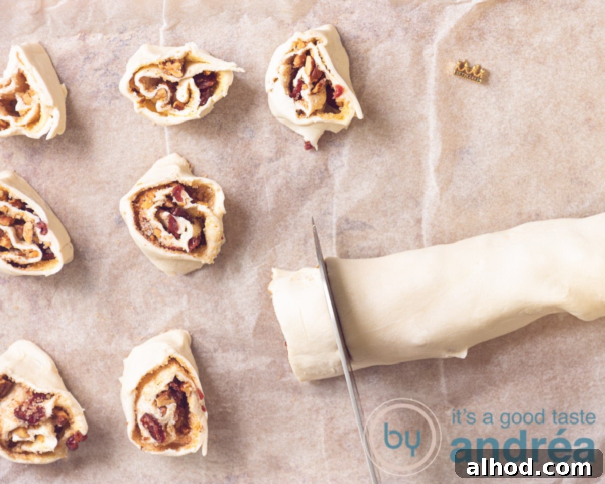 Golden Puff Pastry Cinnamon Buns 6 A rolled log of puff pastry filled with cinnamon, pecans, and cranberries, being cut into individual slices with a sharp knife on a cutting board, revealing the internal spiral.