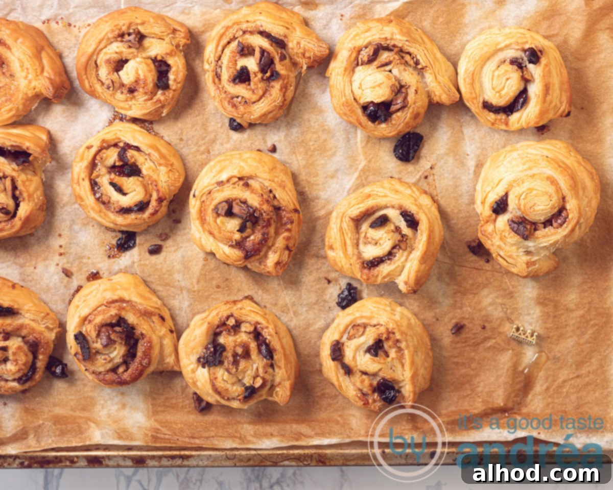 Golden Puff Pastry Cinnamon Buns 7 Freshly baked puff pastry cinnamon rolls with pecans and cranberries on a baking sheet, golden brown and puffed, with a few fresh cranberries sprinkled around.