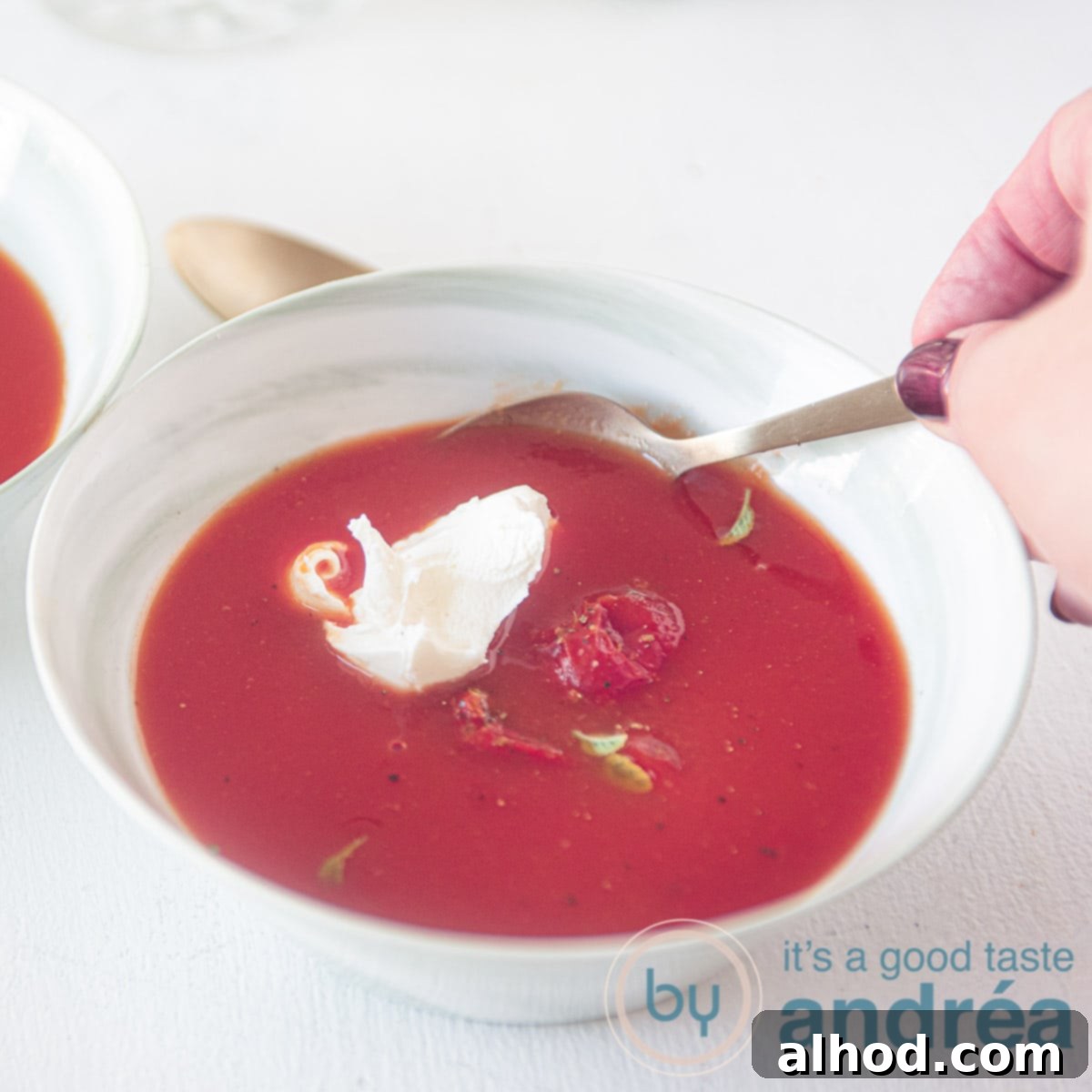 Creamy Tomato Mascarpone Soup 6 Vierkante uitsnede van een kom soep met Italiaanse tomatensoep met mascarpone. Een hand neemt een hap