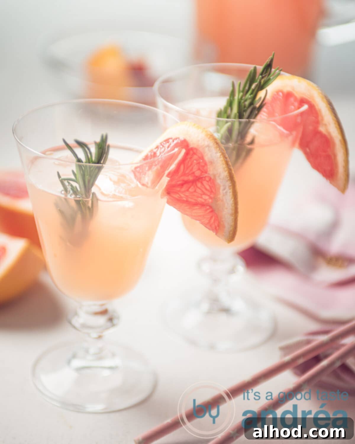 Two vibrant sparkling grapefruit mocktails garnished with fresh rosemary sprigs and grapefruit slices, served with straws, perfect for a summer gathering.