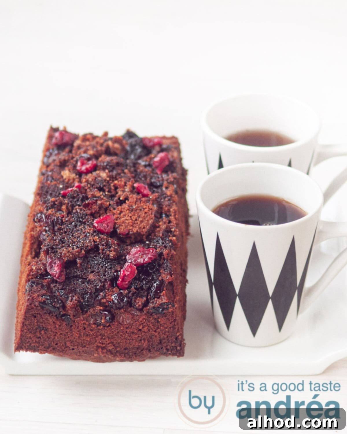 Cake with a caramelized cranberry topping on a white plate and two cups of coffee