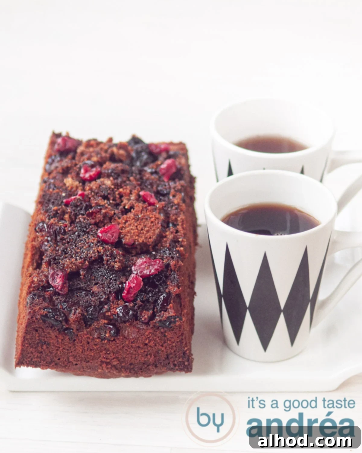 Cake with a caramelized cranberry topping on a white plate and two cups of coffee