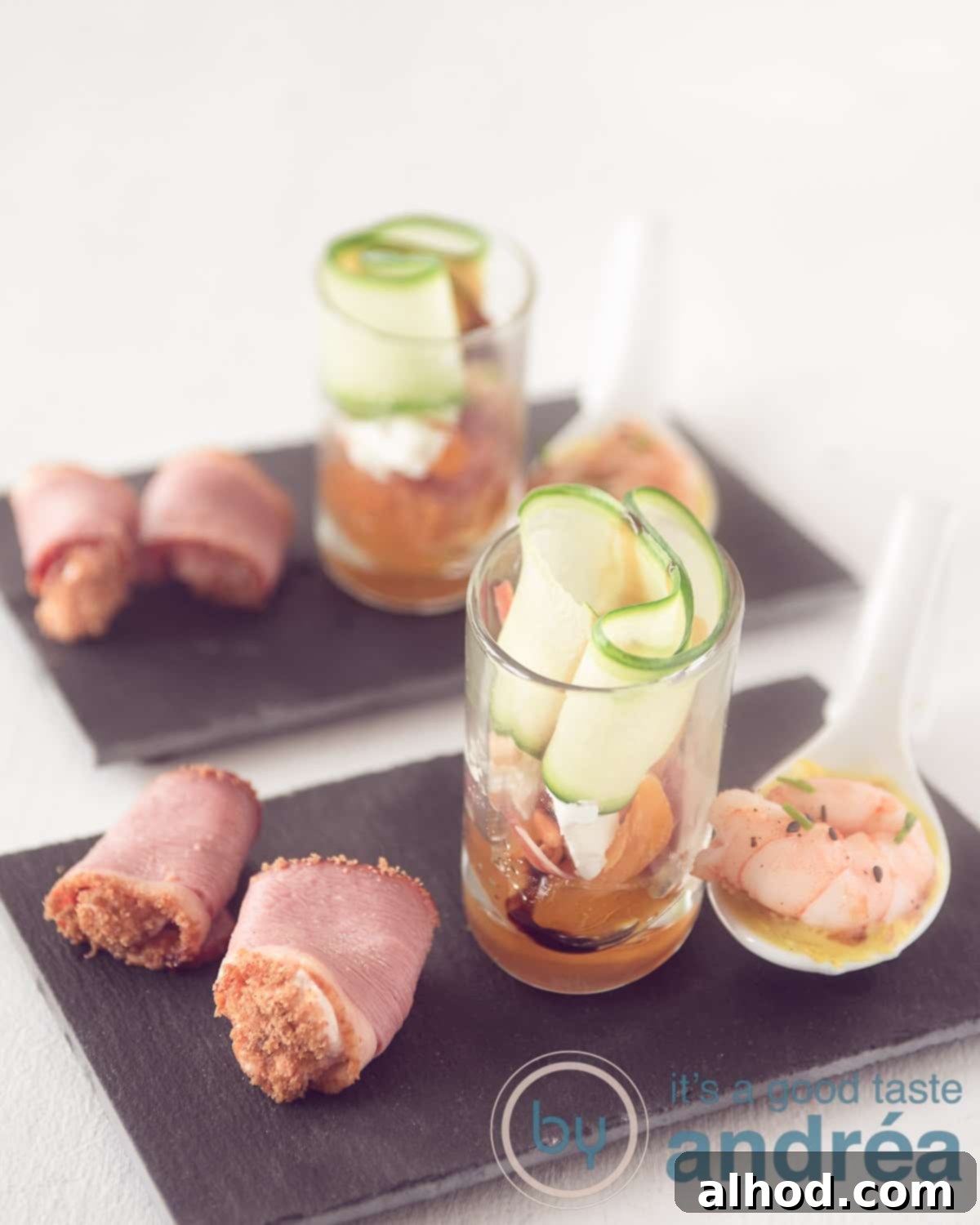 Amuse-Bouche Trio: Ham, Shrimp, Goat Cheese 2 An elevation photo with two times three amuses on a black chalkboard. A spoonful with shrimp, a glass with cucumber and a roll of duck breast.