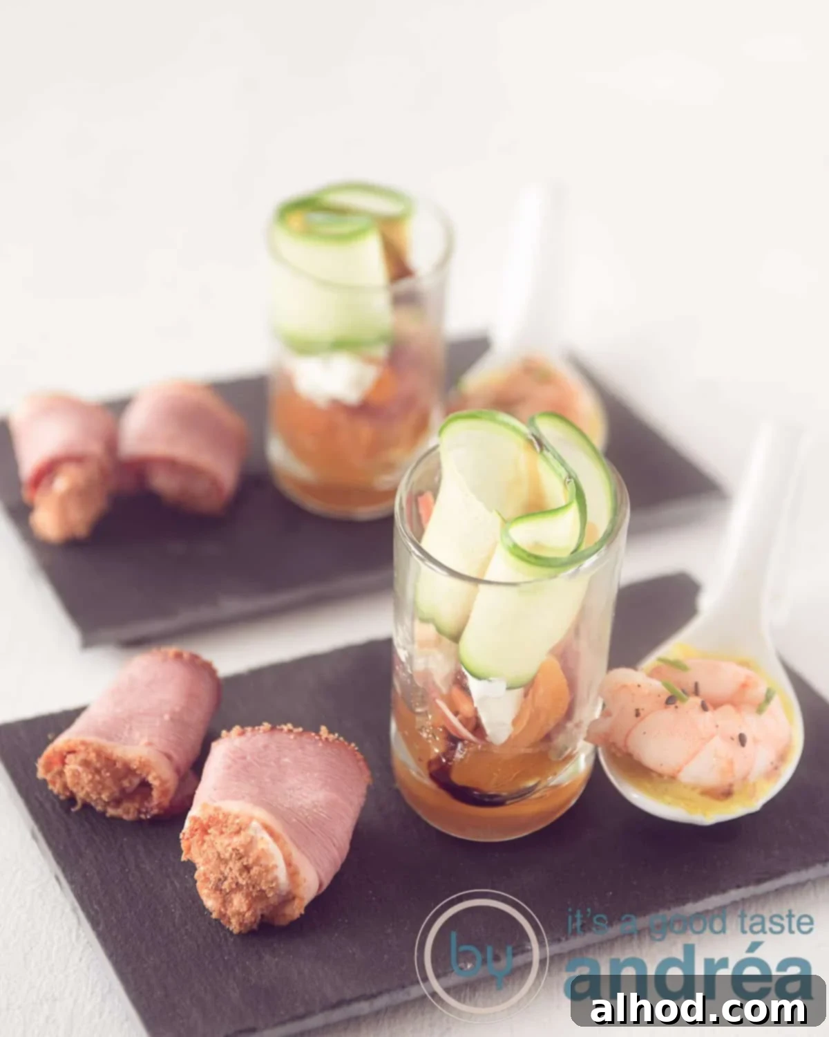 Ham Shrimp and Goat Cheese Amuse Bouche Trio 2 A beautifully arranged black chalkboard displaying three distinct amuse-bouche appetizers: a spoonful of warm chicory and shrimp, a vibrant glass layered with cucumber and a fig-apricot salad, and a rolled duck breast with cream ham. These easy-to-make starters are perfect for any elegant occasion.