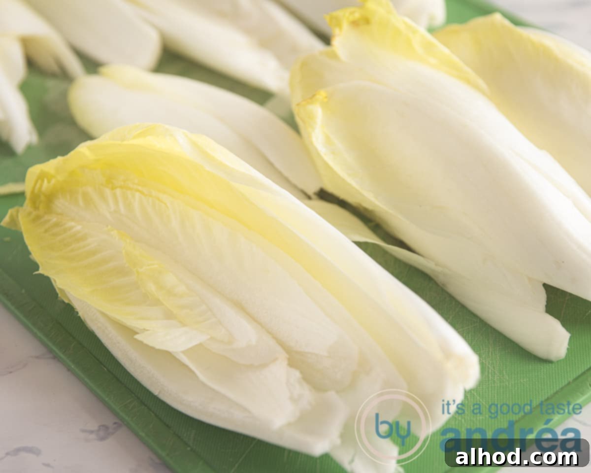 Belgian Endive Bake with Ham and Chevre 4 A close-up image showing a chicory head being halved and its bitter core carefully removed with a knife, illustrating the preparation step.