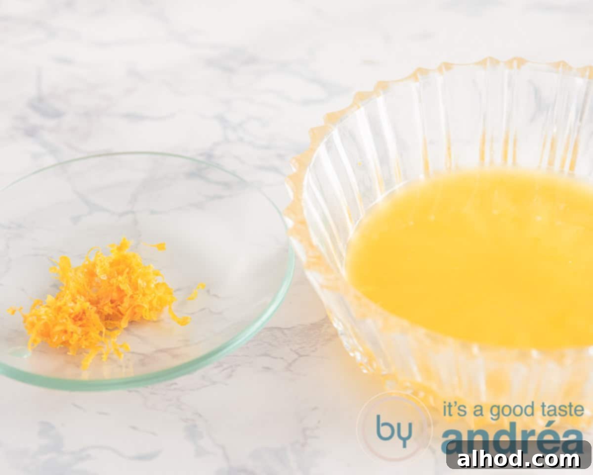 Belgian Endive Bake with Ham and Chevre 5 A close-up of a hand grating orange zest over a bowl, with a juiced orange half next to it, demonstrating the preparation of orange rind and juice.