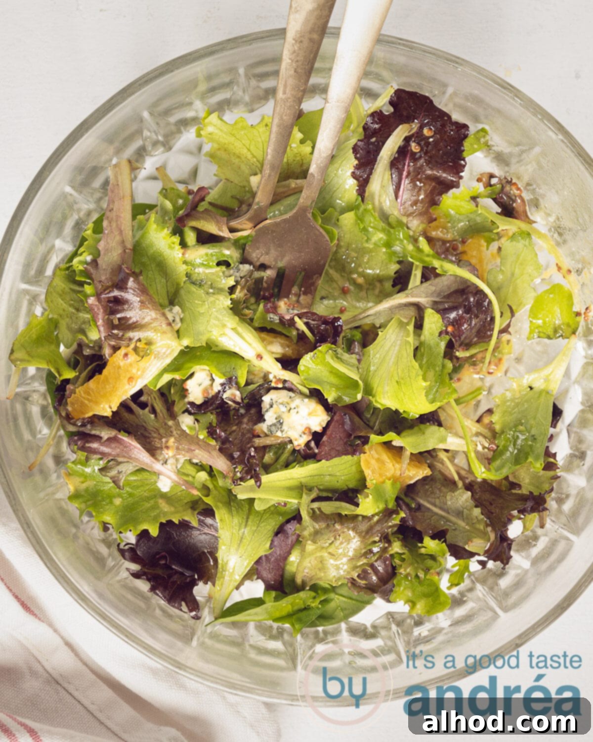 Spicy Blue Cheese Salad with Zesty Orange and Toasted Walnuts 2 A vibrant top-down photo of a glass bowl filled with a mixed green salad, featuring bright orange segments, crumbled blue cheese, and glistening candied walnuts. Two gold forks rest on the side, inviting you to dig in.