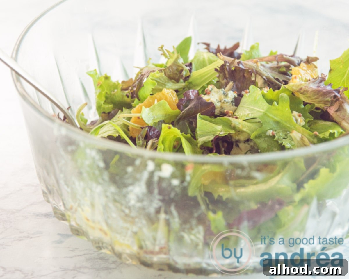 Spicy Blue Cheese Salad with Zesty Orange and Toasted Walnuts 7 A partially assembled salad in a glass bowl, with mixed greens, blue cheese, and orange segments, before the candied walnuts are added.