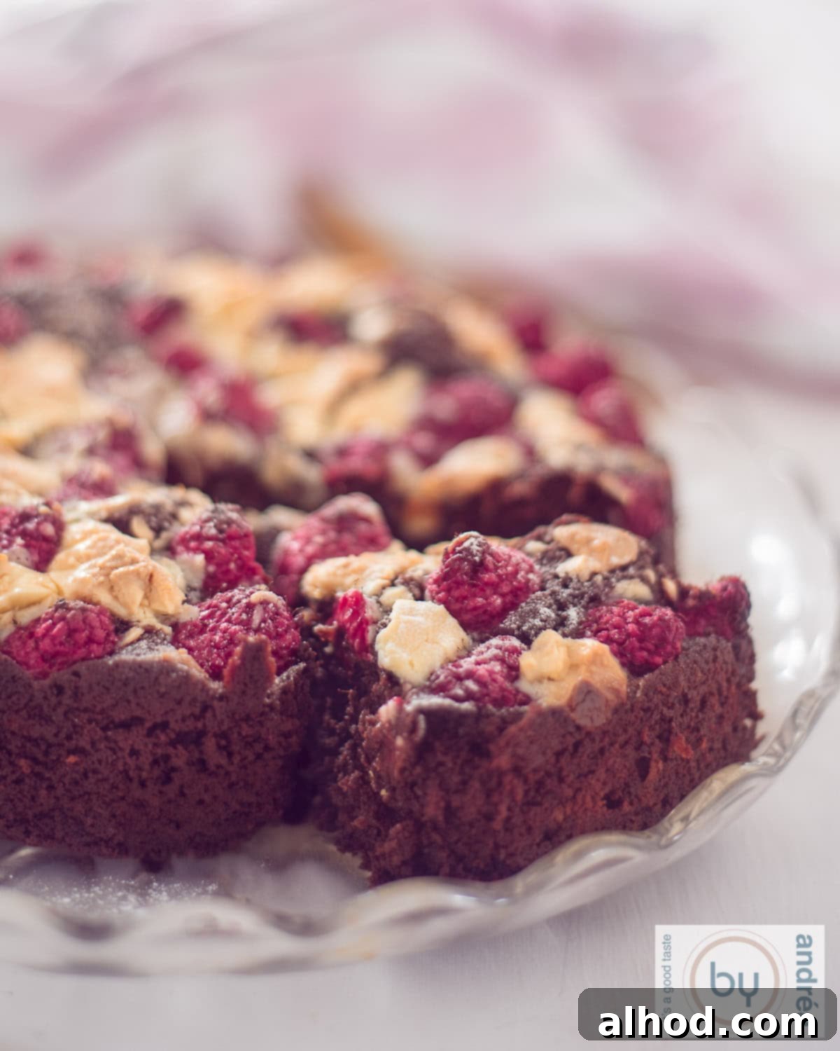 A cake stand with a round brownie cake with pieces of white chocolate and raspberry