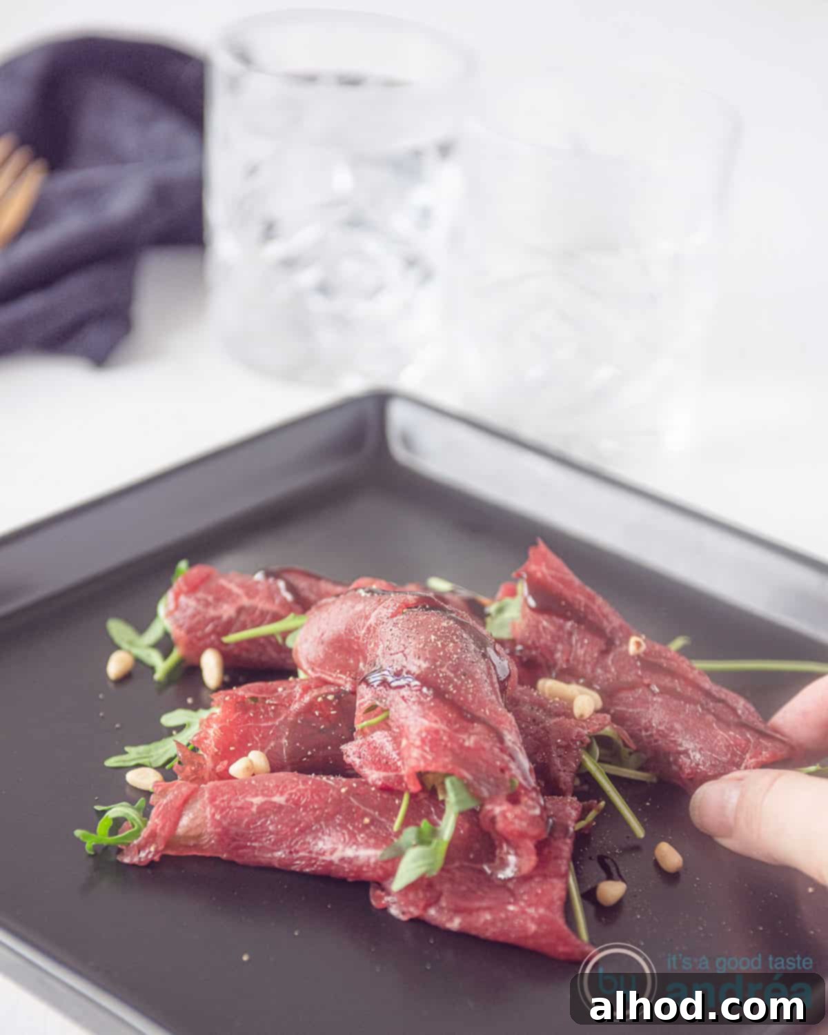 Classic Beef Carpaccio 2 Beef carpaccio roll on a black plate, garnished with arugula and balsamic glaze