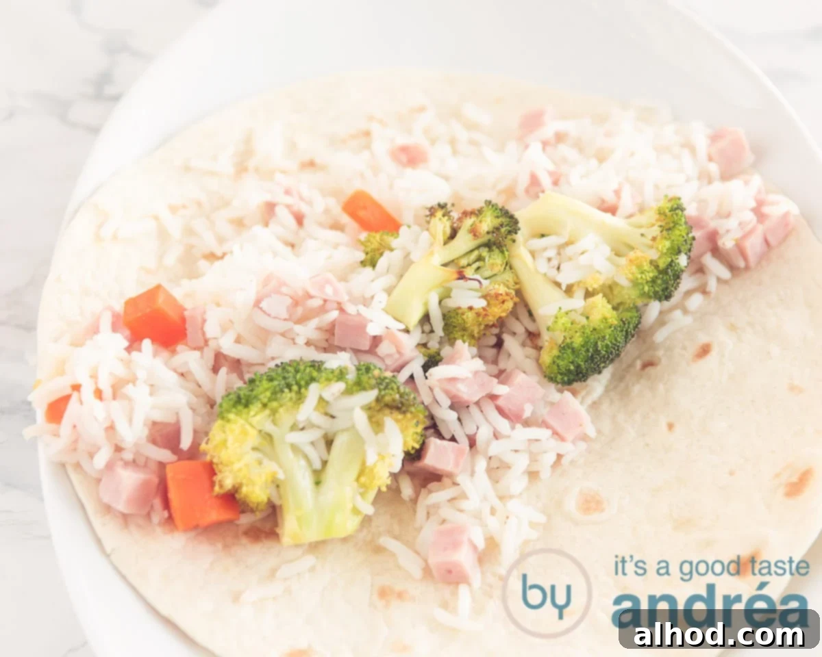 Delicious Ham and Carrot Rice Bake 6 A warm tortilla wrap laid flat on a cutting board with a generous scoop of the rice, carrot, broccoli, and ham filling spread across its center, ready to be rolled