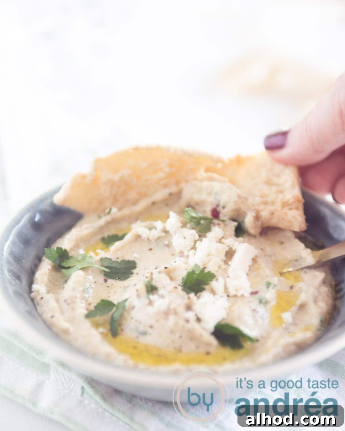 Melitzanosalata: Authentic Greek Roasted Eggplant Dip 7 A hand taking a scoop of the creamy Melitzanosalata dip with a piece of pita bread.