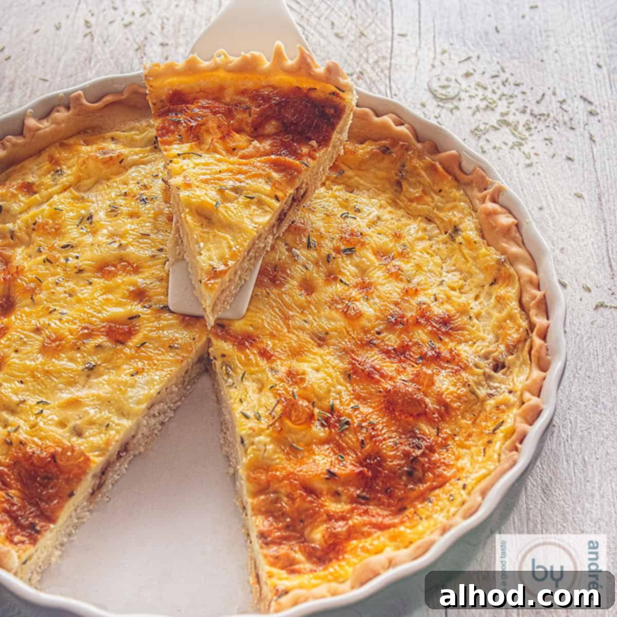 A beautiful vegetarian quiche with shallots and goat cheese, a slice neatly cut and placed on a white cake server, against a simple background.