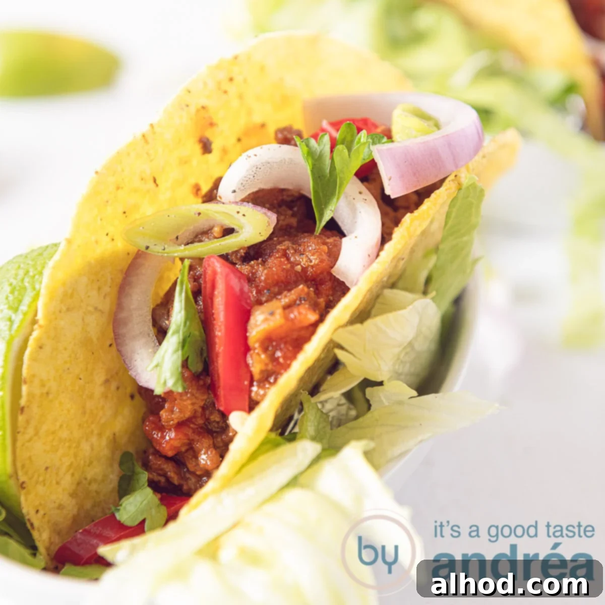 A delicious taco generously filled with hearty chili, garnished with fresh onions and parsley, set against a pristine white background.