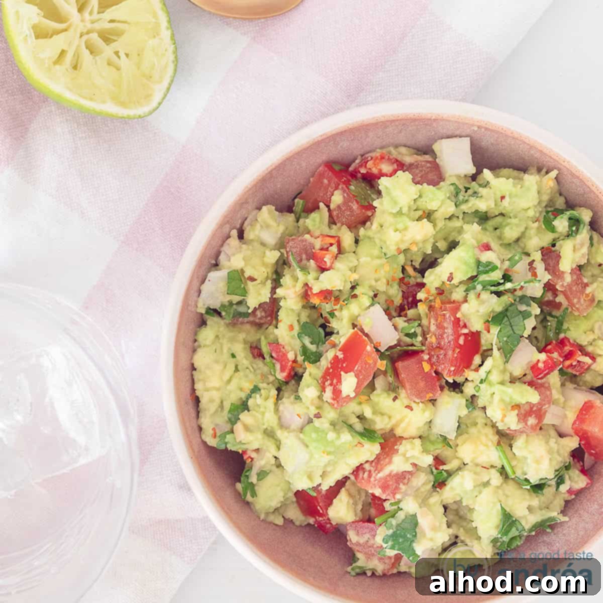 A top-down view of a bowl of freshly made guacamole with vibrant avocado, diced tomatoes, and a wedge of fresh lime, ready for dipping.