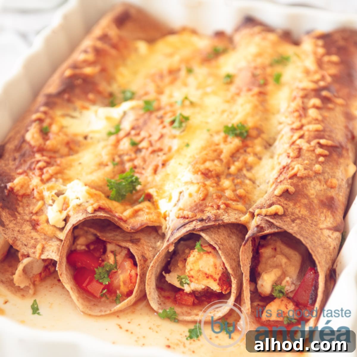 A white baking dish filled with cheesy chicken enchiladas in a creamy tomato sauce, baked to golden perfection.
