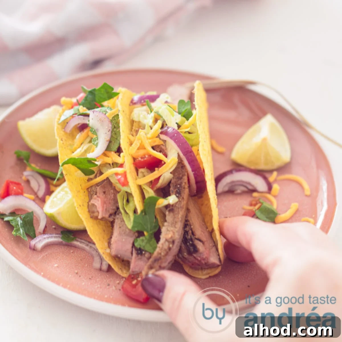 11 Amazing Mexican Recipes to Ignite Your Home Fiesta 8 A vibrant square photo showing a pink plate laden with freshly prepared tacos, generously filled with grilled sirloin steak, crisp fresh vegetables, and topped with shredded Cheddar cheese. A hand is reaching for a taco.
