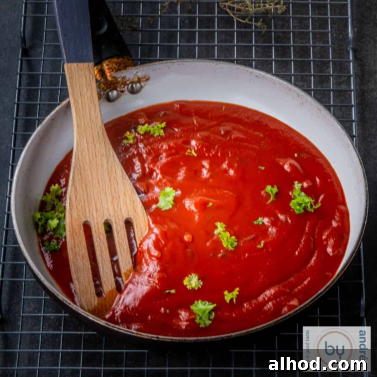 A skillet filled with rich, homemade enchilada sauce, with a wooden spoon resting inside, ready for your Mexican dishes.