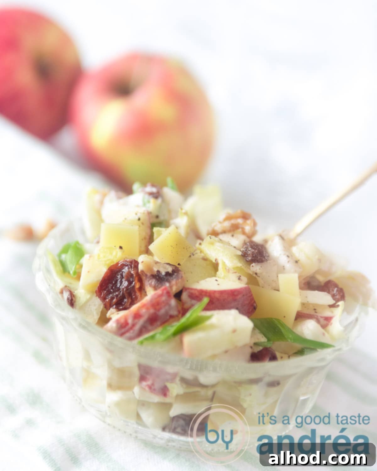 A beautifully arranged bowl of chicory salad with apple, walnuts, and raisins in the foreground. Blurry fresh apples are visible in the background, hinting at the key ingredient.