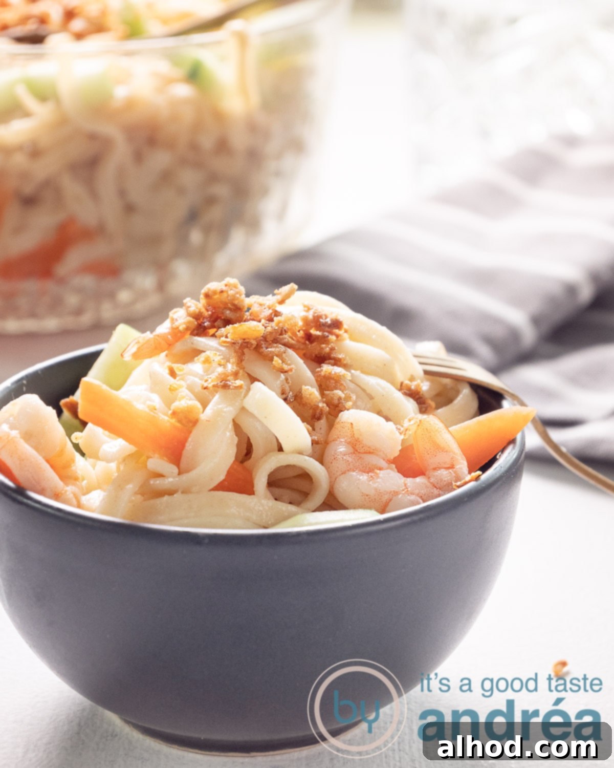Indonesian Noodle Salad with Shrimp 2 A grey bowl filled with Indonesian noodle salad with cucumber, carrot and shrimp. A glass bowl at the back. A grey towel on the right