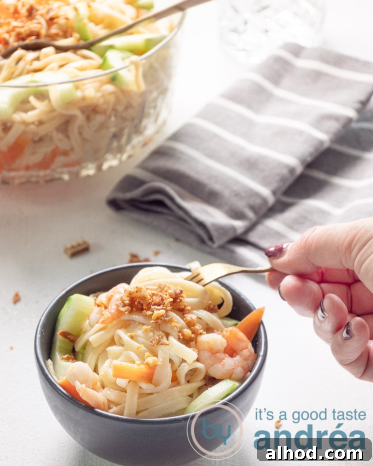 Indonesian Noodle Salad with Shrimp 9 a hand taking a bit of the noodle salad in a great bowl. A big bowl filled with salad and a grey towel are in the back